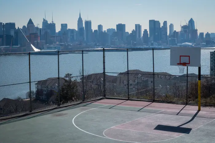 An outdoor basketball court with the New York City skyline in the distance.
